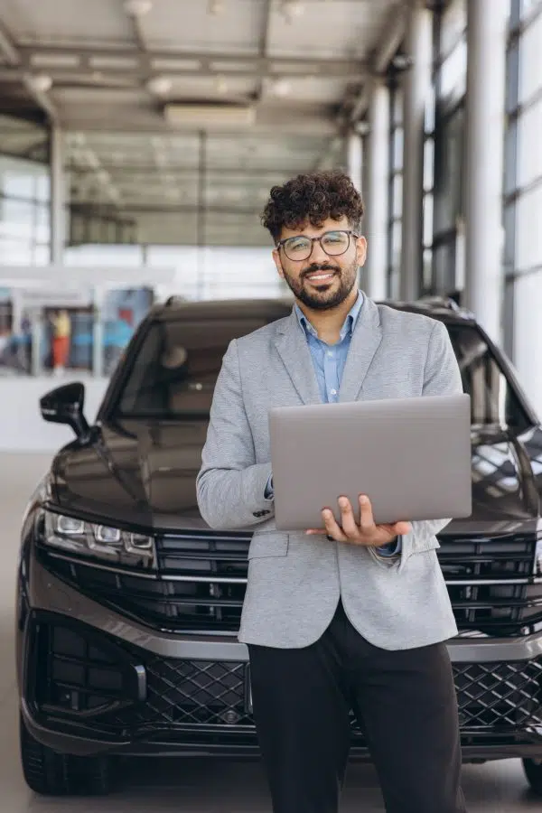 Al Karama Motors vehicle sales consultant holding a laptop beside a black SUV in the Dubai showroom